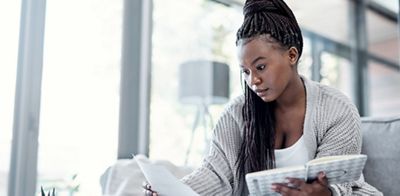 Shot of a young woman going over paperwork on the sofa at home