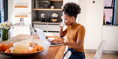 Young woman reading laptop while drinking coffee in her kitchen