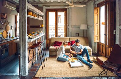 Young couple sitting on floor of living room and eating pizza from box